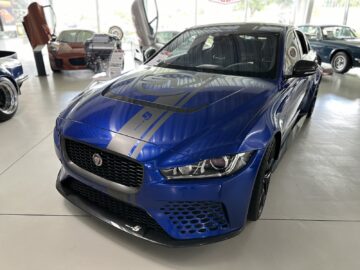 On display inside is a blue Jaguar sports car from the Jaguar Heritage Trust Collection, with a striking hood design and modern details. Other vehicles are visible in the background, adding to the rich tapestry of automotive craftsmanship captured in this reportage.