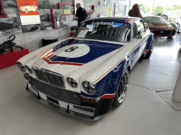 In a showroom, under sharp scrutiny from onlookers, stands proudly a vintage race car from the Jaguar Heritage Trust Collection with the number 8 on the hood. Featuring blue, white and red details, the car attracts attention as if it were straight out of a classic motorsports replica.