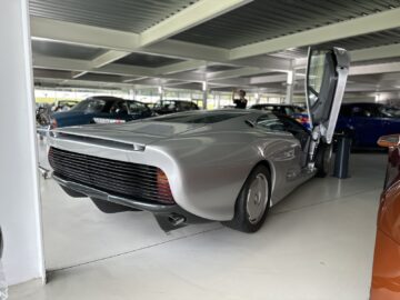 A silver concept car with open wing doors, displayed among other vehicles inside, stands out as a highlight of the Jaguar Heritage Trust Collection.