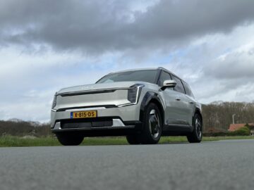 Een zilveren Kia EV9 uit 2024 met Nederlands kenteken X-815-DS staat geparkeerd op een verharde weg onder een bewolkte hemel.