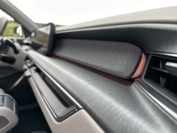 Close-upafbeelding van het dashboard van een Kia EV9 uit 2024 met een grijs stoffen paneel, een zwarte ventilatieopening en een beeldscherm dat op het dashboard is gemonteerd. Het interieur heeft een modern en strak design en weerspiegelt de verfijning die u van een RWD-model verwacht.