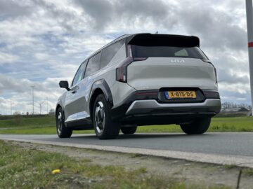 Een witte Kia EV9 SUV uit 2024 met achterwielaandrijving staat geparkeerd langs de weg, tegen de achtergrond van een bewolkte hemel. Op het kenteken van het voertuig staat "X-815-DS.