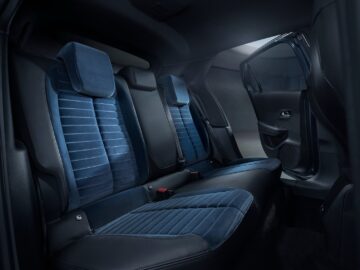 El interior del asiento trasero de un coche con asientos tapizados en azul oscuro con costuras verticales y reposacabezas, con una puerta abierta a la derecha, ejemplifica la promesa premium del Lancia Ypsilon 2024.