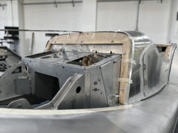 Close-up van een gedeeltelijk geassembleerd metalen carrosserieframe in een werkplaats bij Morgan Motor Company, met houten en metalen componenten waarvan sommige delen aan elkaar zijn geplakt om uit te lijnen. Dit kijkje achter de schermen biedt een exclusief kijkje in het vakmanschap van de auto.