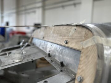 Close-up van een machine met een metalen oppervlak bevestigd met bouten en houten delen vastgezet met tape, die doet denken aan het vakmanschap dat te zien is tijdens een autorondleiding bij de Morgan Motor Company.