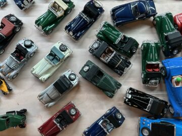 Een verzameling van verschillende vintage speelgoedauto's, meestal in de kleuren groen, blauw en rood, ligt verspreid over een oppervlak. De auto’s zijn gedetailleerd met chromen accenten en verschillende designs.