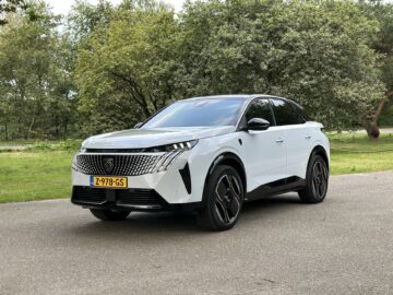 Een wit-zwarte Peugeot E-3008 SUV staat geparkeerd op een verharde weg met bomen en gras op de achtergrond. De auto heeft Nederlands kenteken (Z-978-GS).