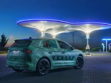 Een elektrisch voertuig van Škoda geparkeerd bij een futuristisch laadstation dat tijdens de schemering met blauwe lichten wordt verlicht.