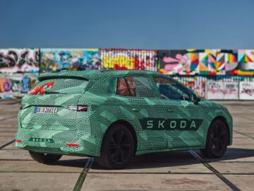Een groene gecamoufleerde Skoda SUV staat op een zonnige dag geparkeerd voor een met graffiti bedekte muur.