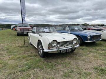 Een witte klassieke cabriolet staat geparkeerd op een grasveld tussen andere vintage voertuigen onder een bewolkte hemel, wat de charme van de West Oxon Steam & Vintage Show 2024 vastlegt. FOTO VERSLAG.