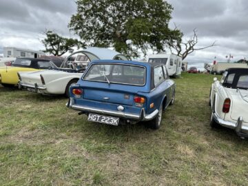 Een blauwe klassieke auto met kenteken HGT 223K staat geparkeerd op een grasveld naast andere oldtimers en kampeertenten tijdens de West Oxon Steam & Vintage Show 2024, zoals vastgelegd in onze FOTOVERSLAG.