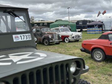 Op de West Oxon Steam & Vintage Show 2024 worden buiten verschillende oldtimers tentoongesteld, met omringende tenten en een bewolkte lucht op de achtergrond. Deze FOTOVERSLAG geeft de nostalgische sfeer van het evenement perfect weer.