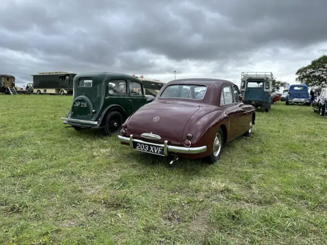 Twee oldtimers staan geparkeerd op een grasveld, omringd door andere klassieke voertuigen op de West Oxon Steam & Vintage Show 2024, onder een bewolkte hemel: een perfect tafereel voor elke FOTOVERSLAG-liefhebber.