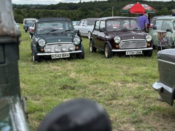 Twee klassieke mini-auto's geparkeerd op een grasveld bij de West Oxon Steam & Vintage Show, met mensen en andere vintage voertuigen op de achtergrond. Bewolkte hemel boven ons, die de essentie van de prachtige FOTOVERSLAG van 2024 vastlegt.