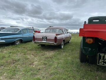 Een oldtimer met kenteken "514 HTM" staat geparkeerd op het gras tussen twee andere klassieke voertuigen onder een bewolkte hemel op de West Oxon Steam & Vintage Show 2024.