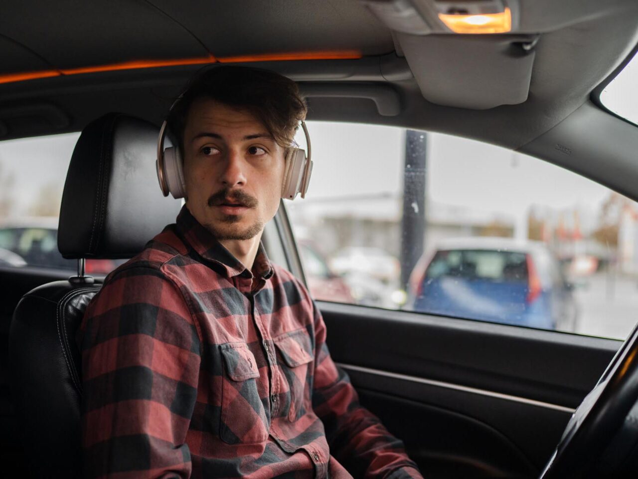 one man adult caucasian male sit in the car with headphones on his head listen t ...