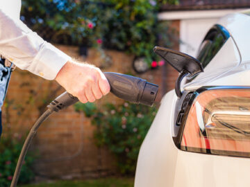Color image depicting a man charging his electric vehicle at home. ...