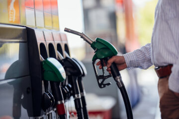 A man in a striped shirt fills up his vehicle at a gas station. He holds a green ...
