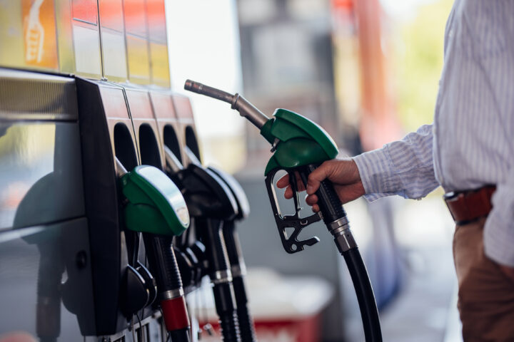 A man in a striped shirt fills up his vehicle at a gas station. He holds a green ...