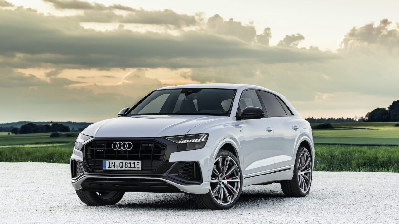 Een witte Audi Q8 TFSI e quattro elektrische SUV geparkeerd op een onverharde weg te midden van een schilderachtig landelijk landschap onder een bewolkte hemel.