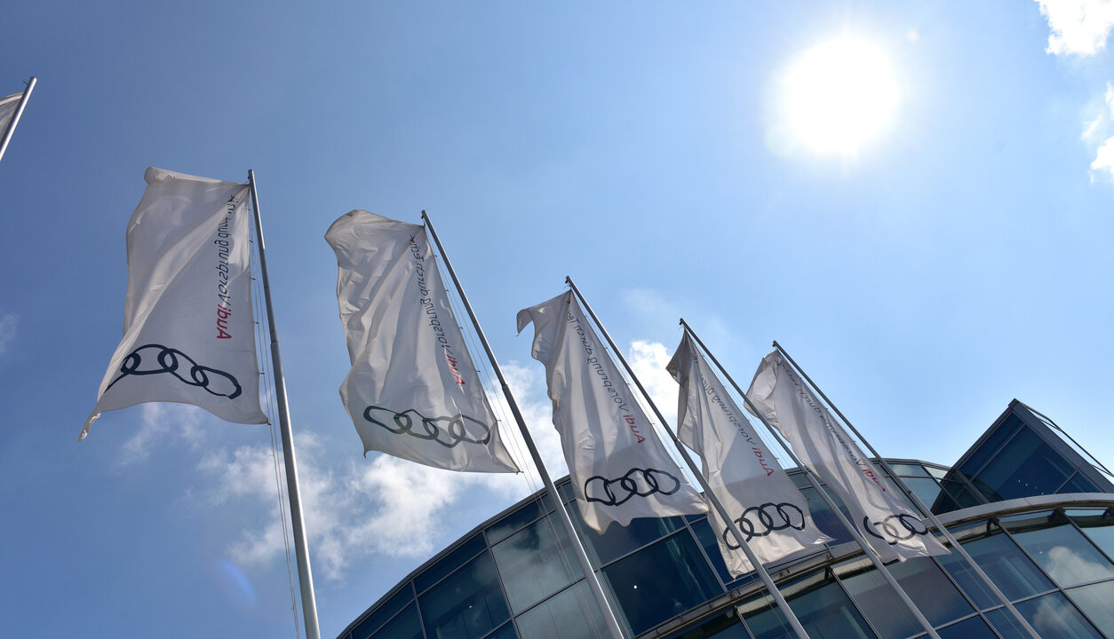 Flags in front of the headquarters of the Audi factory with blue sky and sun in  ...