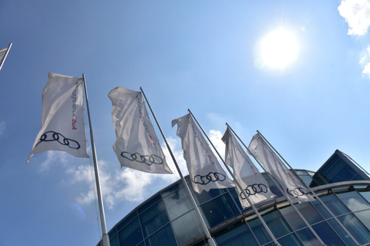 Flags in front of the headquarters of the Audi factory with blue sky and sun in  ...